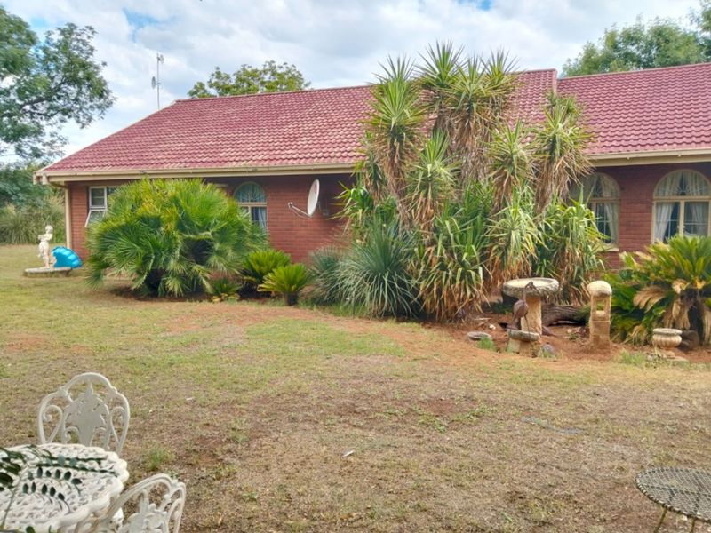 Rear view of a brick farmhouse featuring a tiled roof, arched windows, and an established garden area.