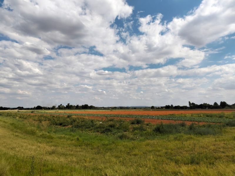 A wide-angle view of expansive, cultivated agricultural fields under a bright, cloudy sky, showcasing the property's rural landscape.