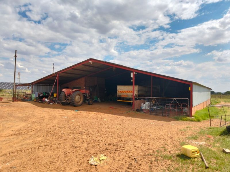 A large, open-sided farm utility barn featuring a steel frame and corrugated metal roof, suitable for equipment storage and agricultural operations.