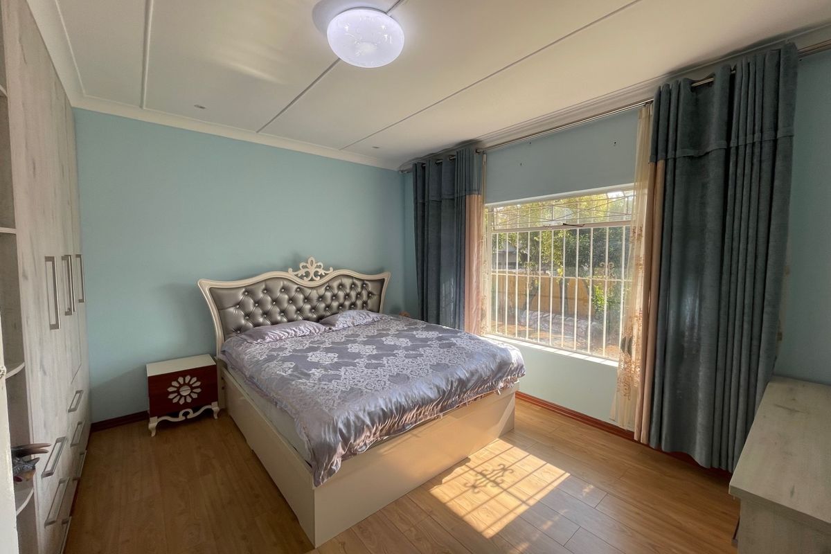 A well-maintained bedroom featuring light blue walls, laminate flooring, a built-in wardrobe, and a window fitted with security bars.