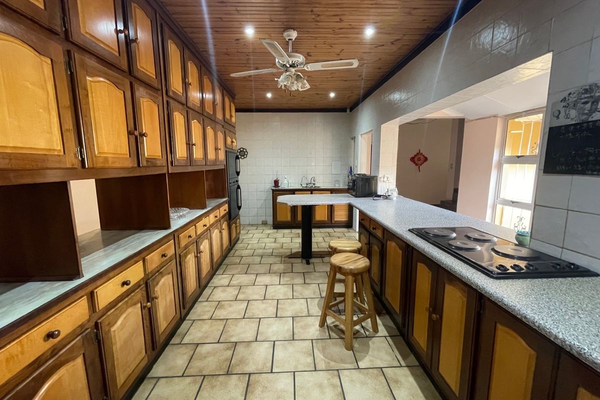Spacious kitchen featuring extensive timber cabinetry, laminate countertops, built-in hob and oven, and a distinctive timber-paneled ceiling with integrated lighting.