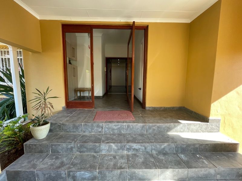 Covered entrance area featuring tiled steps leading to a timber-framed glass door and a view into the interior hallway.