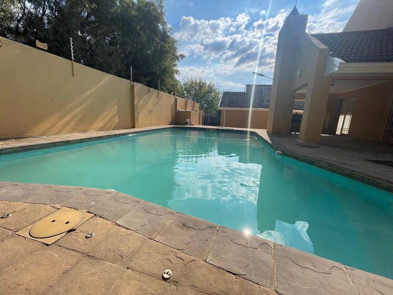 A well-maintained swimming pool area featuring paved surrounds, a perimeter wall with electric fencing, and an adjacent covered patio.