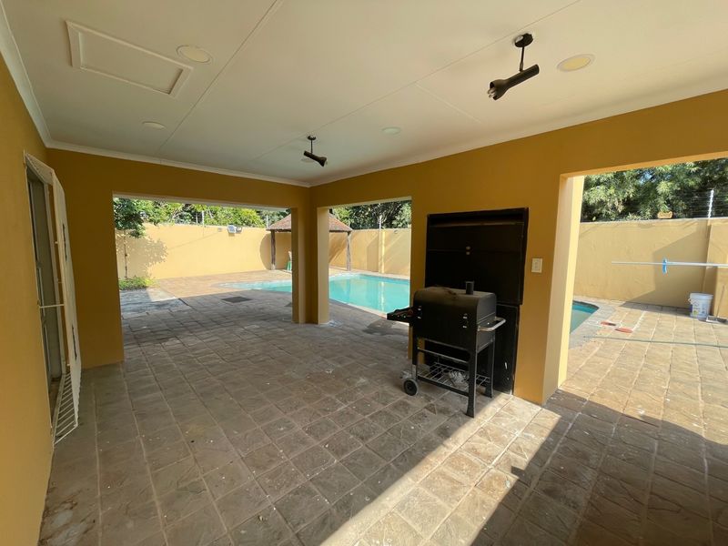 Covered outdoor patio featuring a built-in braai, paved flooring, and direct access to the swimming pool area.