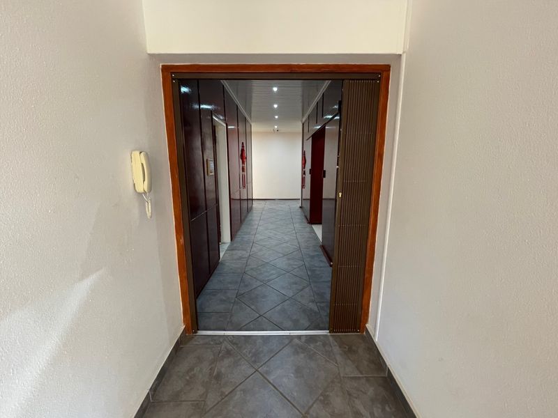 A clean, tiled hallway featuring recessed ceiling lighting and a sliding security gate, providing access to the interior living spaces.