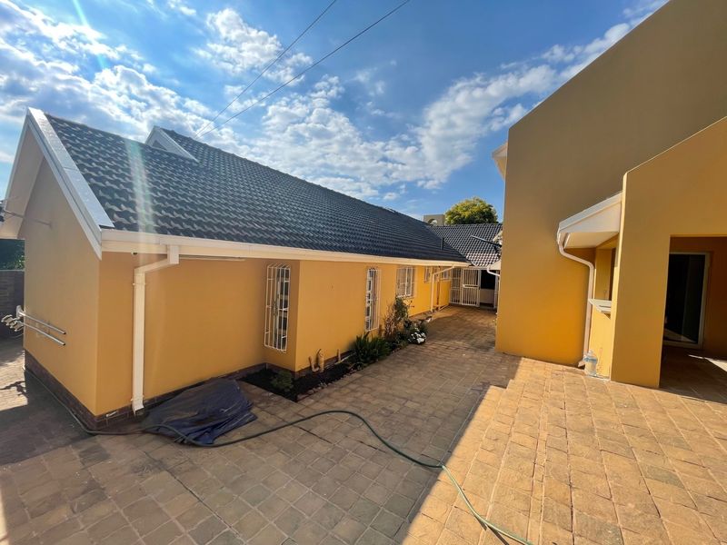 A view of the rear exterior of the property featuring a paved courtyard area, tiled roofing, and secure window bars.
