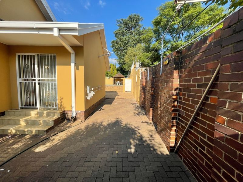 A side exterior view showing a paved walkway, brick boundary wall with electric fencing, and access to the rear garden area.