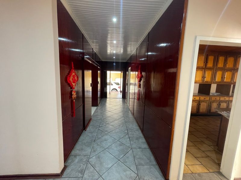 A spacious hallway featuring tiled flooring, dark wood wall paneling, and recessed ceiling lights, providing a clear transition between living areas.