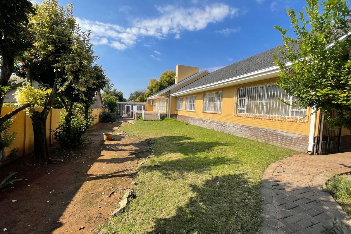 A view of the rear exterior of the house featuring a lawn, paved walkway, and secure windows with metal bars.