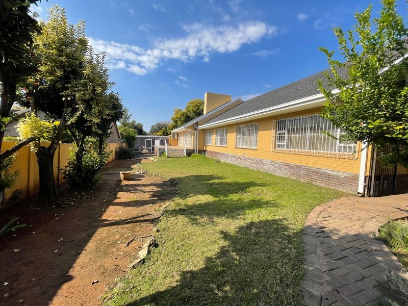 A view of the rear exterior of the house featuring a lawn, paved walkway, and secure windows with metal bars.