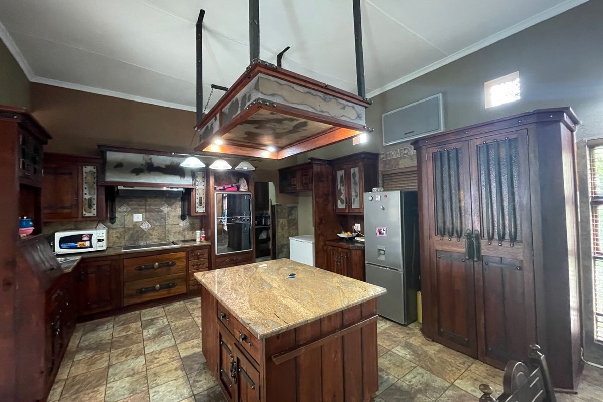 Spacious kitchen featuring custom dark wood cabinetry, a central granite-topped island, built-in appliances, and tiled flooring with a rustic aesthetic.
