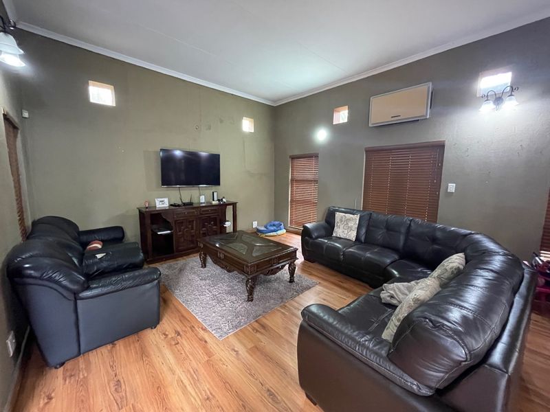 Spacious living room featuring laminate flooring, wall-mounted air conditioning, and wooden blinds, offering a functional layout with neutral wall tones.