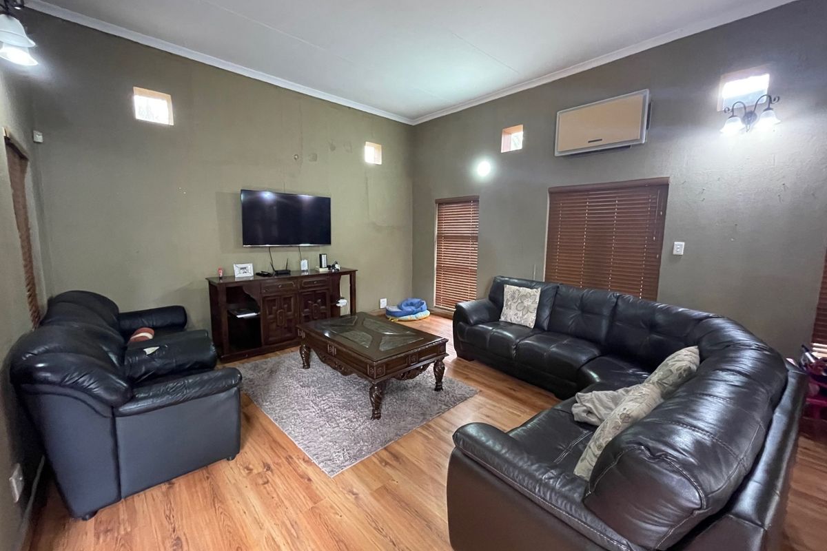 Spacious living room featuring laminate flooring, wall-mounted air conditioning, and wooden blinds, offering a functional layout with neutral wall tones.