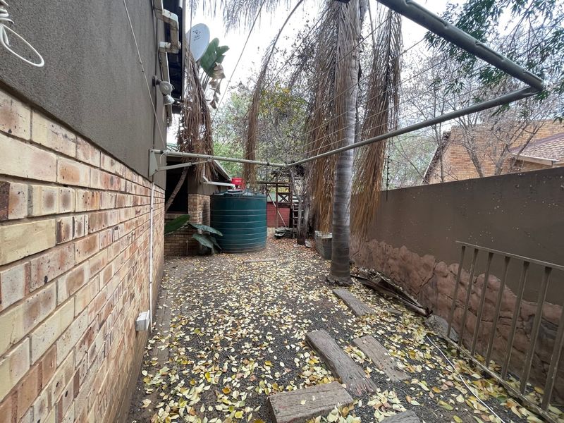A rear exterior area featuring a water storage tank, rotary clothesline, and brick boundary wall with electric fencing.