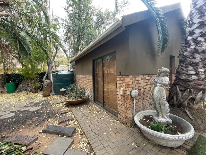 Rear exterior view of the property featuring a brick facade, sliding glass door access, and a paved walkway leading through the garden area.