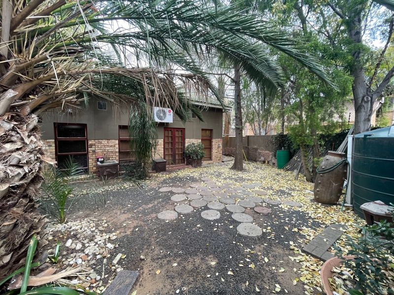 Rear garden area featuring a brick facade, air conditioning unit, water storage tank, and paved stepping stones set within a landscaped yard.