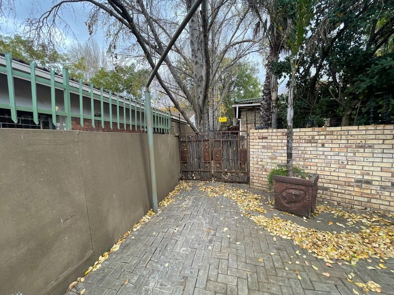 A paved rear courtyard area featuring a brick boundary wall, metal security gate, and integrated security camera.
