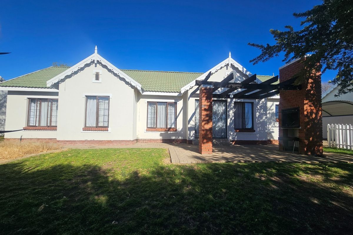 Rear view of the townhouse featuring a paved patio, built-in braai, pergola, and a well-maintained garden area.