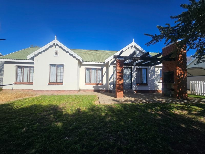 Rear view of the townhouse featuring a paved patio, built-in braai, pergola, and a well-maintained garden area.