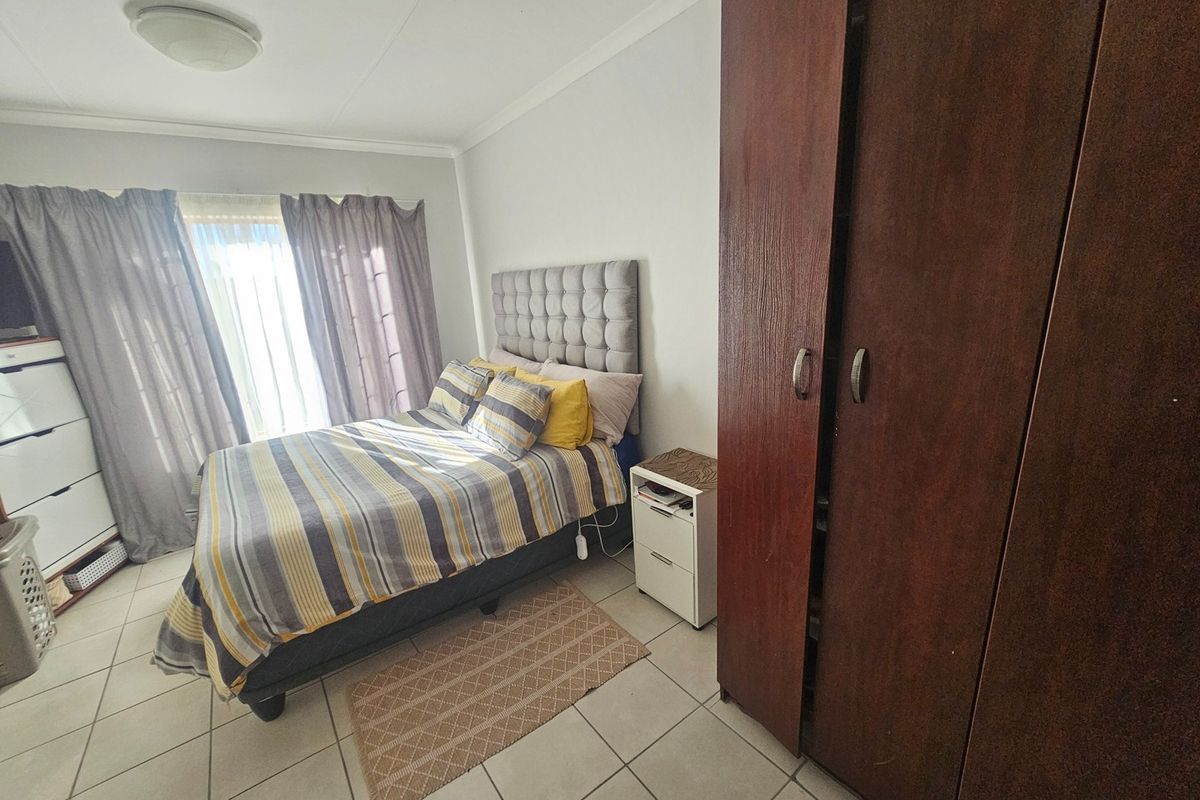 A functional bedroom featuring tiled flooring, a built-in wardrobe, and natural light through the window.