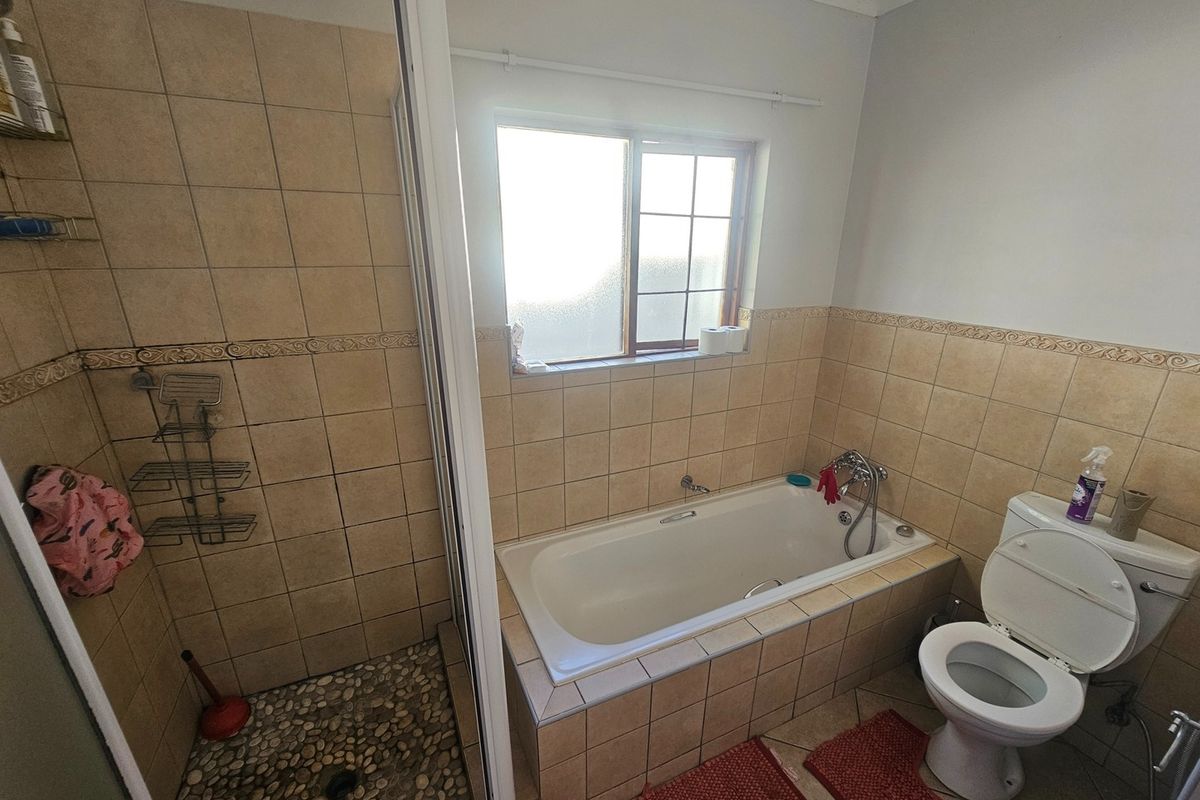 A functional bathroom featuring a built-in bathtub, a separate shower enclosure with pebble flooring, and tiled wall finishes.