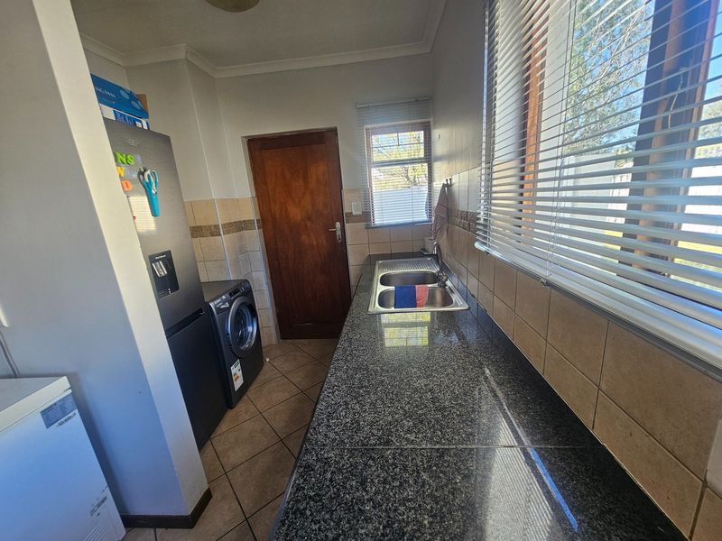 Functional scullery area featuring granite countertops, a double stainless steel sink, tiled splashbacks, and ceramic floor tiles with direct access to an exterior door.