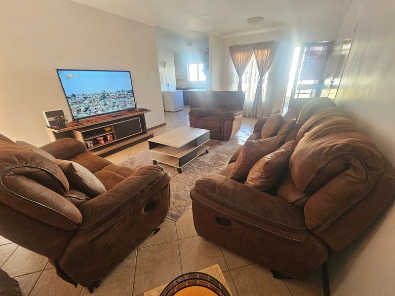 Open-plan living area featuring tiled flooring and direct access to an outdoor space, with a view through to the kitchen area.