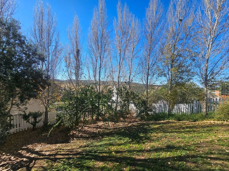 A private garden area featuring mature trees and a white picket fence, offering a peaceful outdoor space.