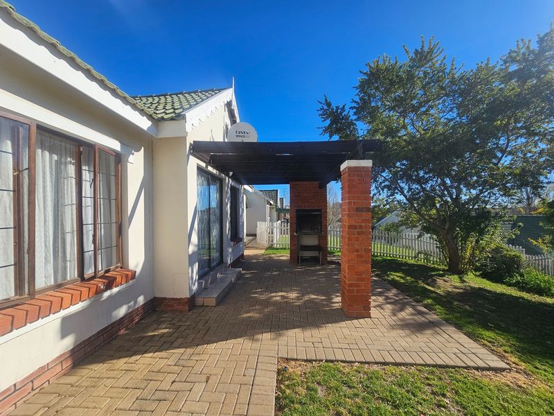 A paved outdoor patio area featuring a built-in brick braai and a timber pergola, providing a functional space for outdoor entertaining.