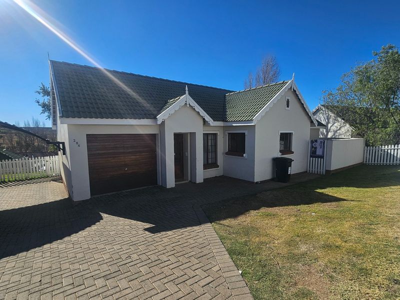 Front elevation of a townhouse featuring a tiled roof, single garage, paved driveway, and a white picket fence.