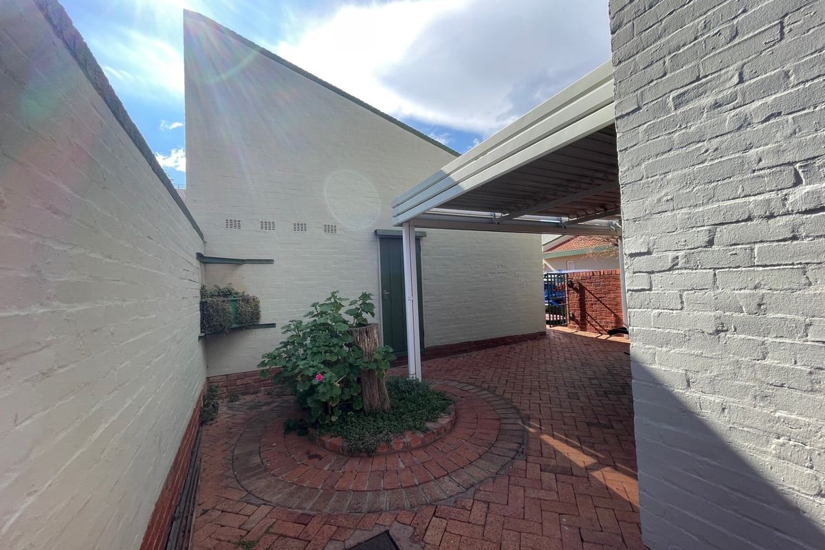 A private rear courtyard featuring brick paving, a covered carport area, and painted brick walls.