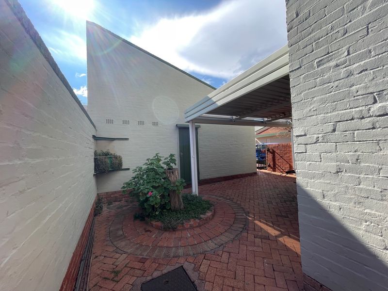 A private rear courtyard featuring brick paving, a covered carport area, and painted brick walls.