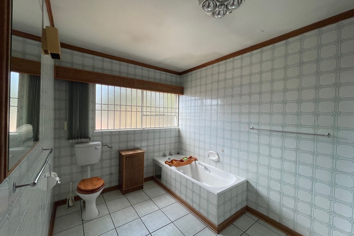 A dated bathroom featuring original tiled walls, a built-in bathtub, and a standard toilet, offering significant potential for a modern renovation.