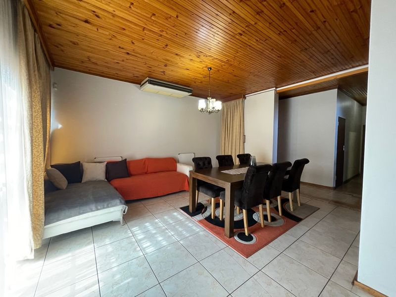 Open-plan living and dining area featuring ceramic floor tiles, a timber tongue and groove ceiling, and a wall-mounted air conditioning unit.