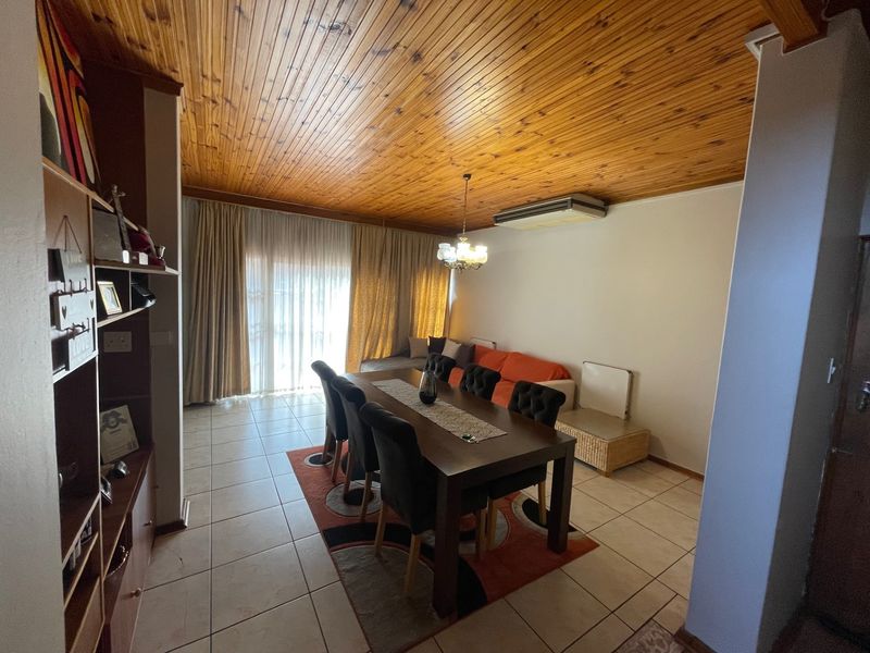 A living and dining area featuring a distinctive timber tongue and groove ceiling, tiled flooring, and a ceiling-mounted air conditioning unit.