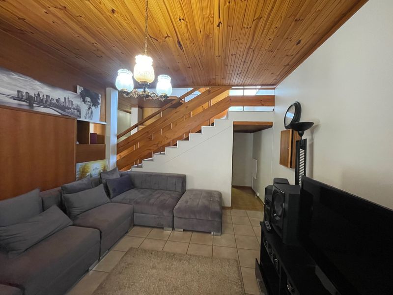 Living room featuring a timber tongue and groove ceiling, ceramic tiled flooring, and a prominent timber staircase.