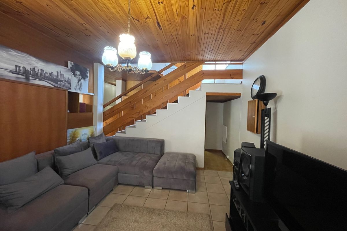 Living room featuring a timber tongue and groove ceiling, ceramic tiled flooring, and a prominent timber staircase.