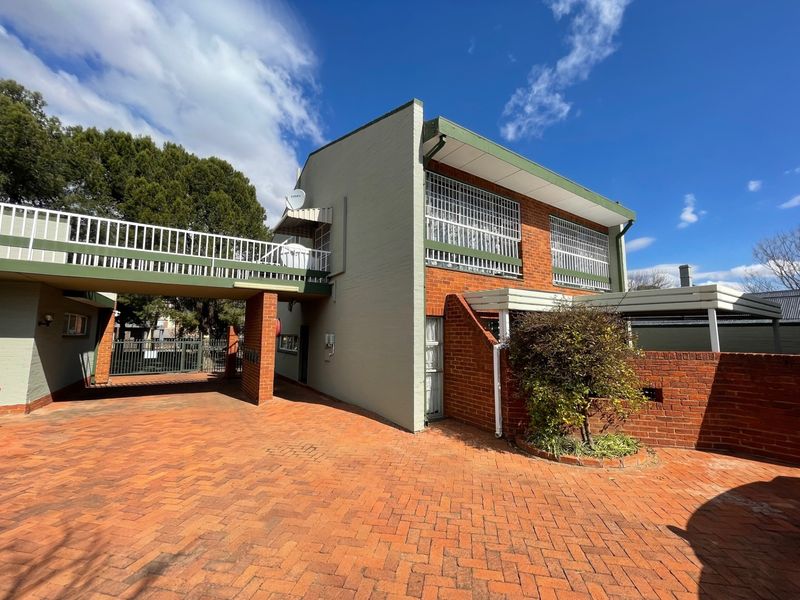 Front exterior view of a townhouse complex featuring brick paving, a covered elevated walkway, and secure window bars.