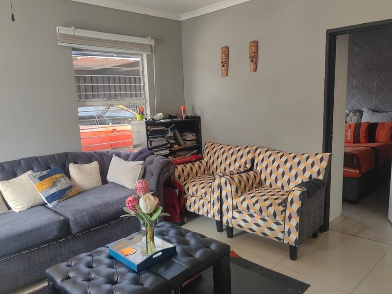 A living room area featuring tiled flooring, a window with security bars, and neutral wall finishes, providing a functional space for relaxation.