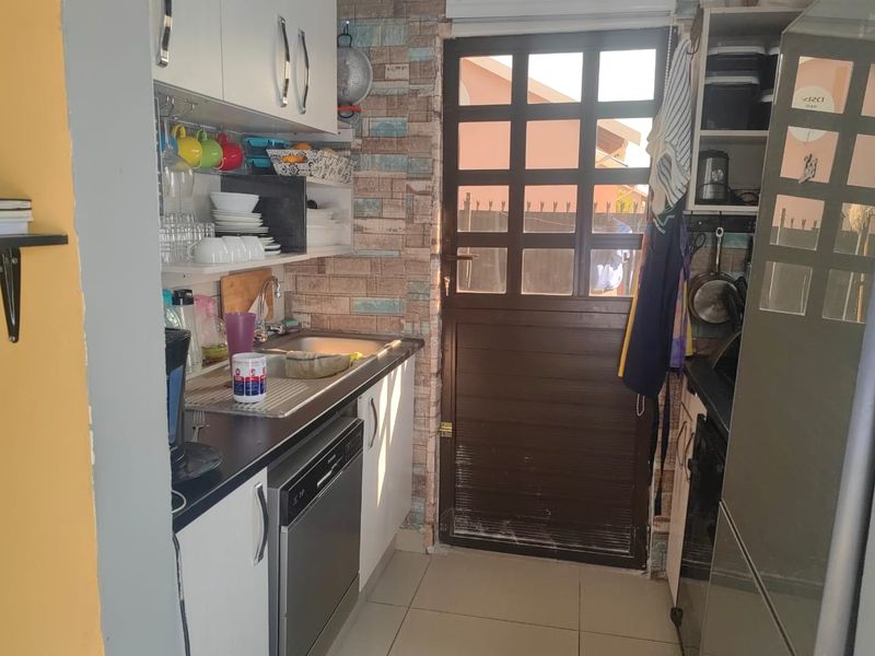 Compact scullery area featuring built-in cabinetry, a stainless steel sink, integrated dishwasher, and decorative brick-effect wall finishes with direct access to the exterior.