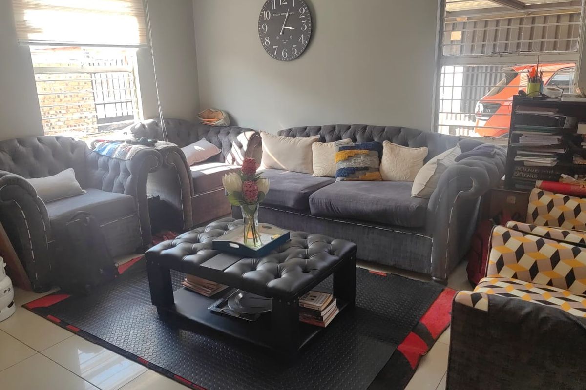 A comfortable living room featuring tiled flooring, large windows with security bars, and roller blinds, providing a functional and well-lit space.