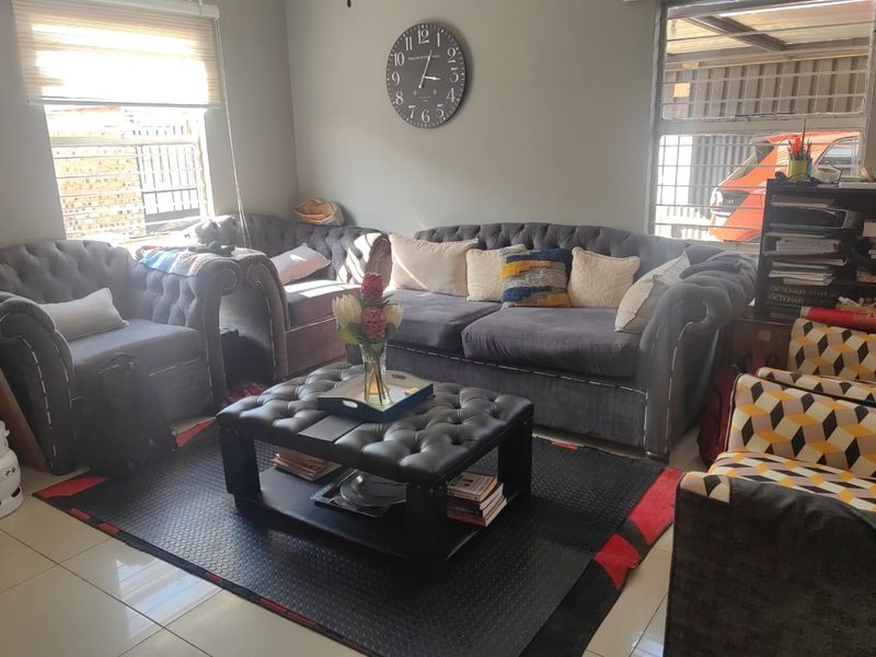 A comfortable living room featuring tiled flooring, large windows with security bars, and roller blinds, providing a functional and well-lit space.