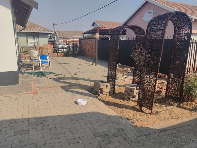 A rear exterior view of the property featuring a paved courtyard area, brick boundary walls, and metal gate access.