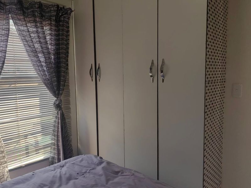 A bedroom featuring a built-in wardrobe with white doors and metal handles, complemented by a window with venetian blinds.