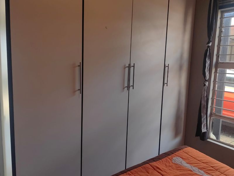 A bedroom featuring a large built-in wardrobe with modern handles and a window fitted with security bars.
