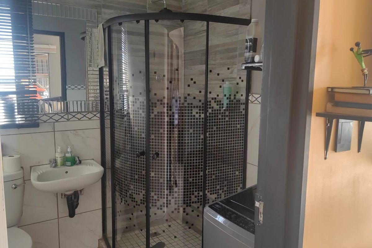 A compact bathroom featuring a corner shower enclosure, wall-mounted basin, toilet, and decorative tiled wall finishes.