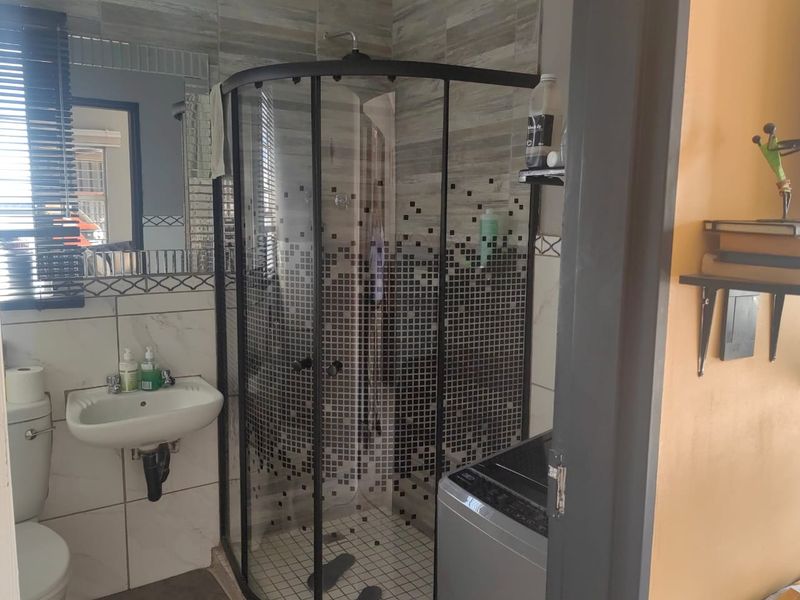 A compact bathroom featuring a corner shower enclosure, wall-mounted basin, toilet, and decorative tiled wall finishes.