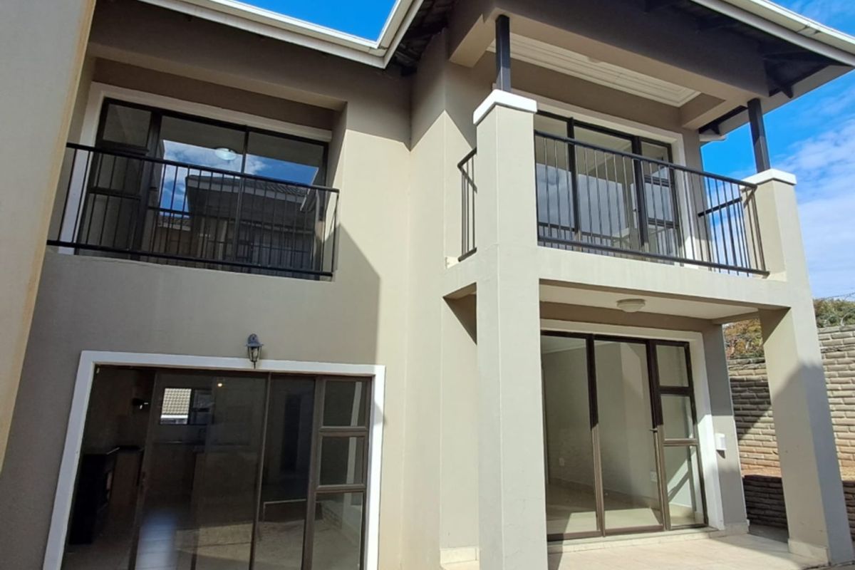 Rear view of a modern townhouse featuring a paved patio, ground floor sliding doors, and an upper-level balcony with metal railings.