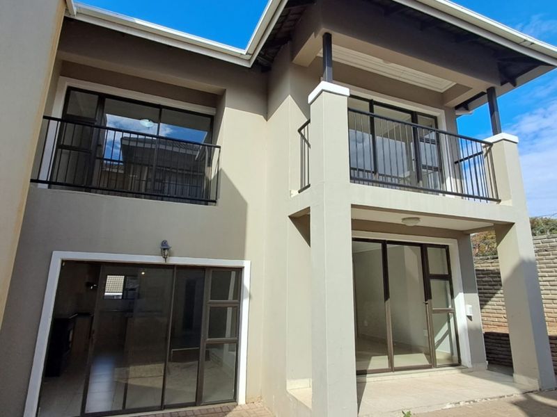 Rear view of a modern townhouse featuring a paved patio, ground floor sliding doors, and an upper-level balcony with metal railings.