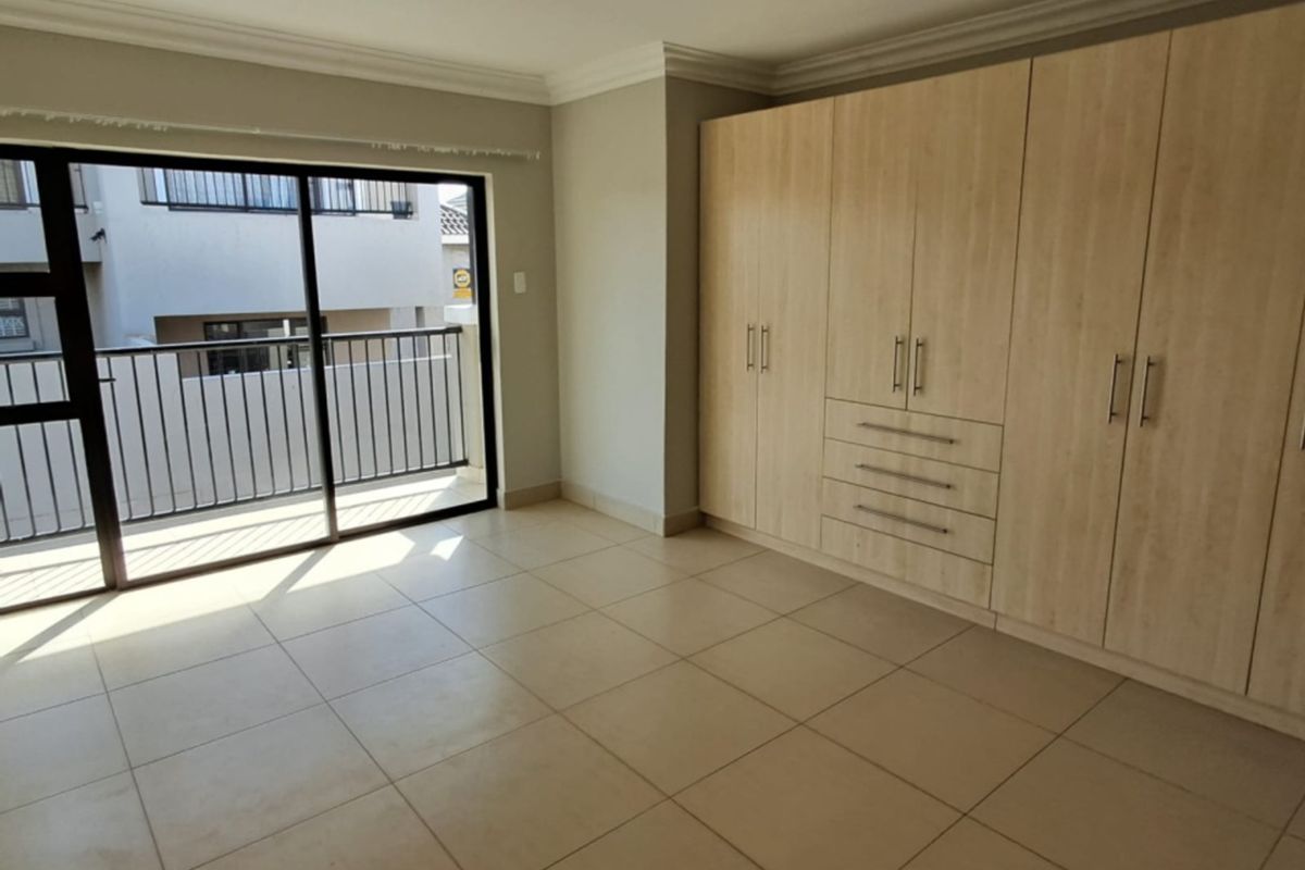Spacious bedroom featuring neutral tiled flooring, extensive built-in cupboards, and a sliding glass door providing access to a private balcony.